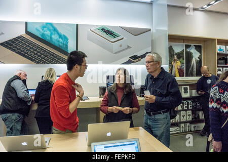 senior couple hover over a laptop & listen intently to young salesman in Apple store at upscale Las Encantadas Shopping Center Stock Photo