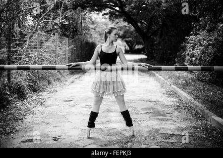 A beautiful young blond ballerina is standing on her toes in front of a boom gate.This photo is black and white Stock Photo