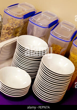 Breakfast cereals in plastic containers and white china bowls stacked up in a communal eating area Stock Photo