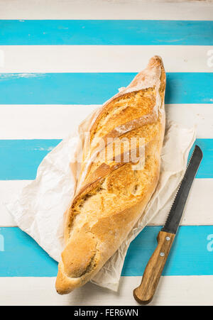 Loaf of bread on a grocery paper bag (european style) on a rustic mediterranean white and blue wooden table.