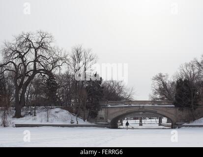 A man and dog walk underneath a bridge on frozen lake of the Isles in Minneapolis, Minnesota, US. Stock Photo