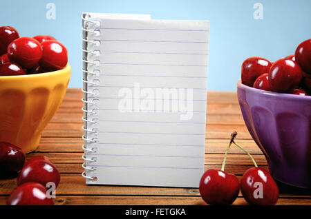Bowl with cherries fruit and notepad on blue background Stock Photo