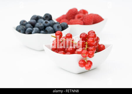 Redcurrants, Raspberries and Blueberries in white bowls on a white background. Stock Photo