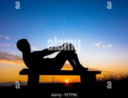 Jogger warming up doing sit ups at sunset in woodland park. UK Stock Photo
