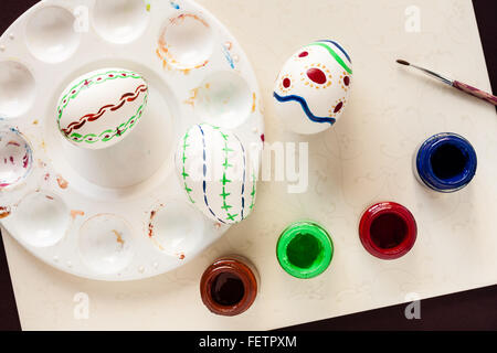 Natural white eggs with various patterns painted by hand for Easter with art supplies. Festive background with natural light. Stock Photo