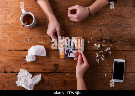Sad mans, womans hands holding torn picture of romantic couple. Stock Photo
