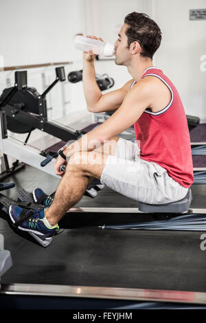 Muscular man on rowing machine drinking water Stock Photo