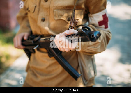 Unidentified woman reconstructor dressed as a Soviet military nurse with a submachine gun in hand. Close up on hands Stock Photo