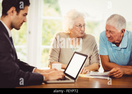 Businessman using laptop while senior couple is reading documents Stock Photo