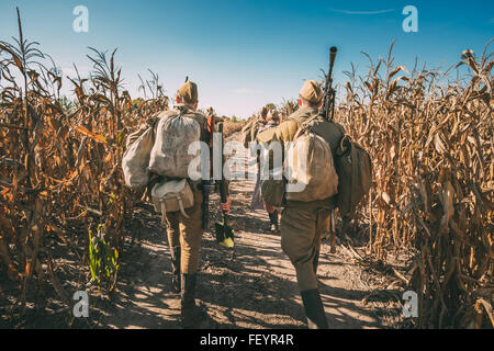 Group of unidentified re-enactors dressed as Soviet russian soldiers goes along field road. Stock Photo