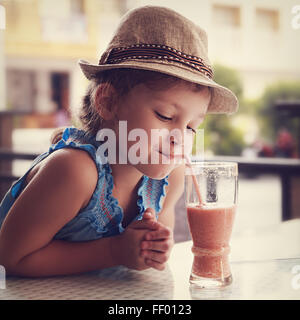 Cute thinking kid girl drinking tasty juice in street restaurant. Toned closeup portrait Stock Photo