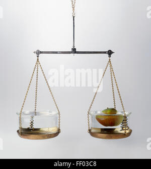 Set of scales with a bowl of water and a bowl containing an apple on it, illustrating Archimedes' principle Stock Photo