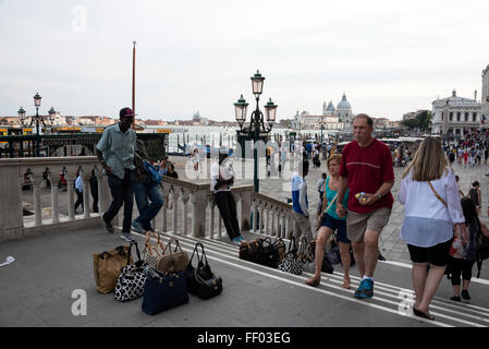 An African immigrant illegal street vendor selling counterfeit ladies handbags such as Gucci, Fendi and Prada to tourists in a busy tourist area of Stock Photo