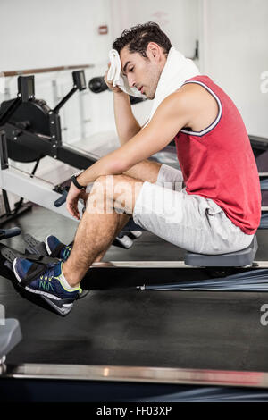 Muscular man on rowing machine wiping sweat with towel Stock Photo