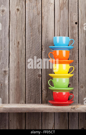 Colorful coffee cups on shelf against rustic wooden wall with copy space Stock Photo