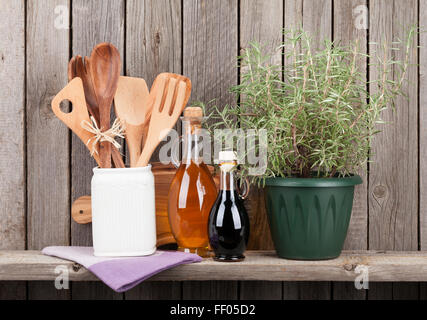 Kitchen utensils, herbs and spices on shelf against rustic wooden wall Stock Photo