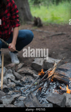 A person is seen kindling a fire at a campsite, preparing for a night of warmth and light. The flickering flames provide a sense of comfort and safety in the outdoor setting, with the campfire serving as the focal point of the camping experience. Stock Photo