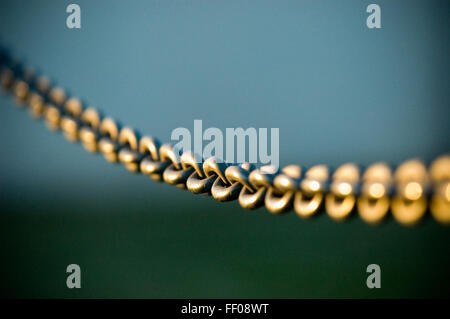 A close-up of a minimalist metal chain with interlocking links, set against a blurred blue background. The design emphasizes simplicity and modern aesthetics. Stock Photo