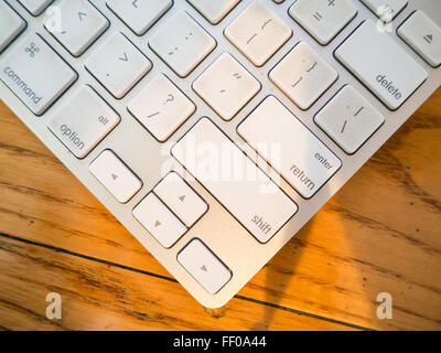 A grey keyboard with flat keys, designed for a streamlined, modern aesthetic. The flat keycaps feature standard letters, option, and shift keys, making it ideal for both office and casual computing. The wood grain surface contrasts with the sleek keyboard design. Stock Photo