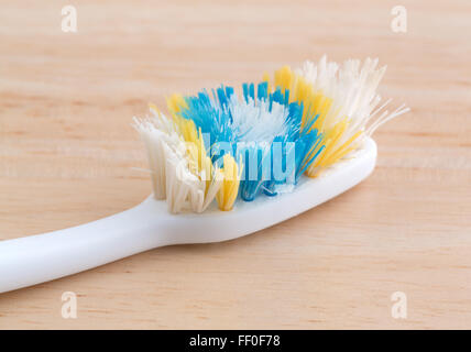 An old worn toothbrush with bent bristles on a wood counter top illuminated with natural light. Stock Photo