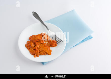 A small portion of spicy flavored pink salmon on a plate with fork atop a blue napkin and off white tablecloth Stock Photo