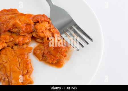 Close view of a small portion of spicy flavored pink salmon on a plate with fork atop an off white tablecloth Stock Photo