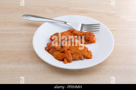 Side view of a small portion of spicy flavored pink salmon on a plate with fork atop a wood table top illuminated with natural l Stock Photo