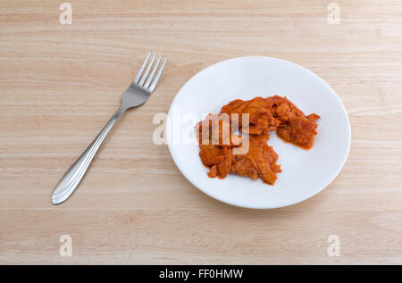 Top view of a small portion of spicy flavored pink salmon on a plate with fork to the side atop a wood table top Stock Photo