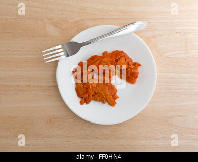 Top view of a small portion of spicy flavored pink salmon on a plate with fork atop a wood table top illuminated with natural li Stock Photo