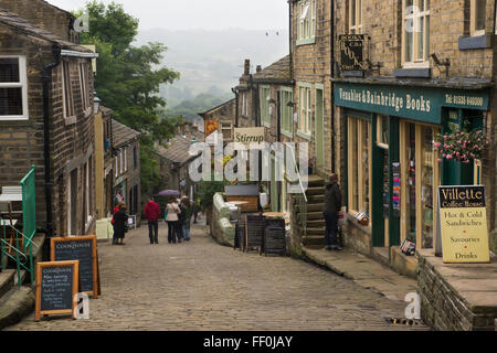 People walk down the steep Main Street, Haworth, West Yorkshire, England - quaint, cobbled, lined with shops, popular with Bronte Country visitors! Stock Photo