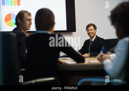 Group of business people meeting in corporate conference room, smiling during a presentation. The coworkers are examining charts Stock Photo