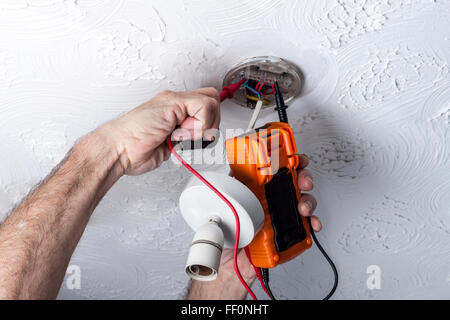 Electrician testing  a ceiling mounted light fitting with a multimeter Stock Photo