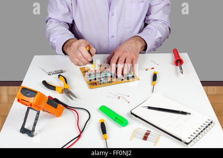 Electronic test engineer using a screwdriver to mount a circuit board switch on his white topped work bench Stock Photo