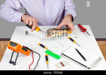 Electronic test engineer using long nose pliers mount component in a circuit board on his white topped work bench Stock Photo
