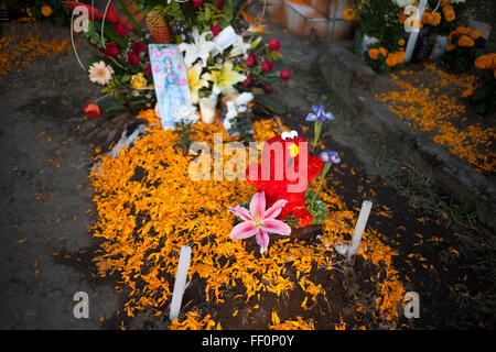 A red teddy bear made with flower petals and yellow marigold flowers, known as cempasuchil, decorate a tomb at a cemetery Stock Photo