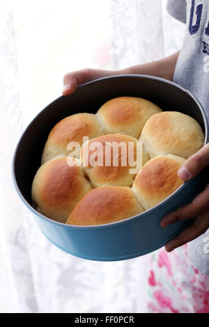 Child hand holding home made baked buns in baking tin Stock Photo