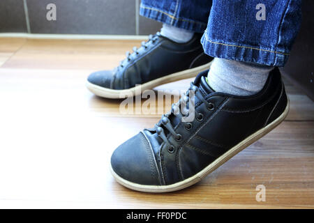 Child's leg in blue jeans and  black shoes on wooden floor Stock Photo