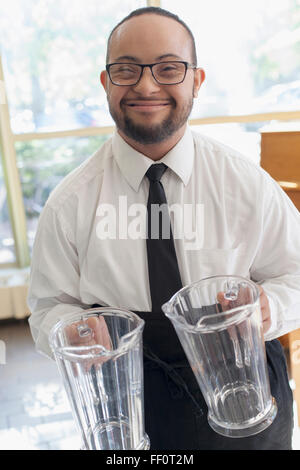 Mixed race server with down syndrome holding pitchers in restaurant Stock Photo