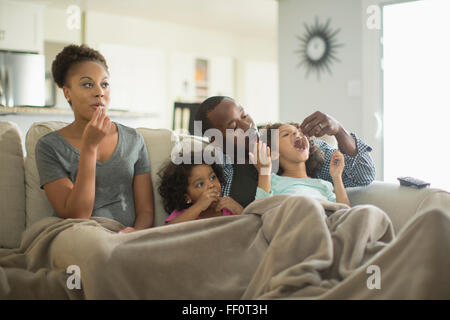 Family in blanket snacking on sofa Stock Photo