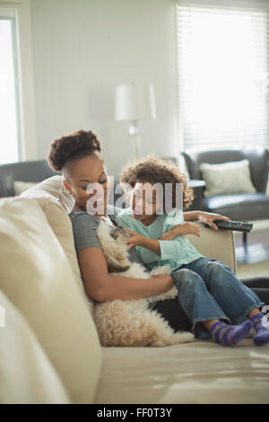 Mother and daughter petting dog on sofa Stock Photo