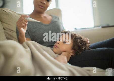 Mother measuring temperature of daughter on sofa Stock Photo