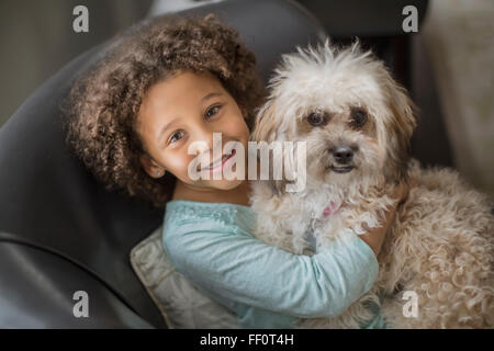 Mixed race girl petting dog on sofa Stock Photo