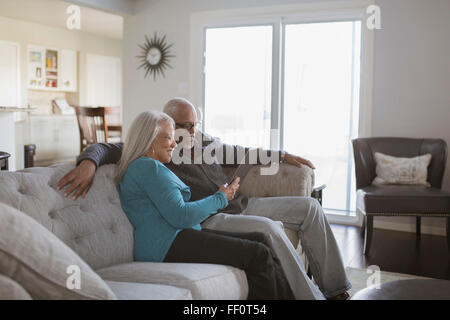 Older couple using digital tablet on sofa Stock Photo