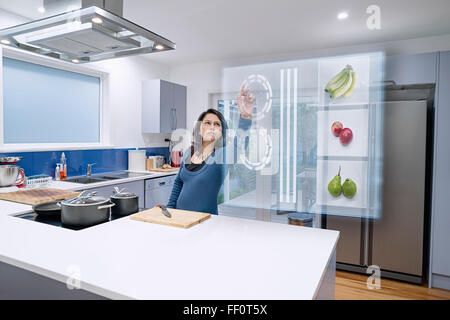 Mixed race woman using holographic screen in kitchen Stock Photo