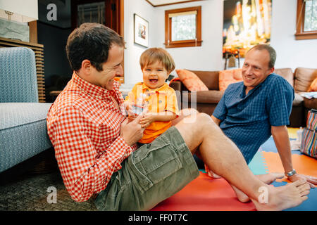 Gay fathers playing with baby son in living room Stock Photo
