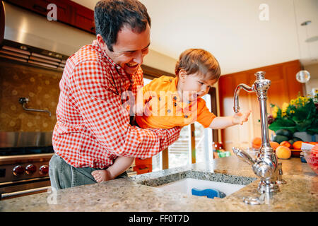 Father and son playing with faucet in kitchen Stock Photo