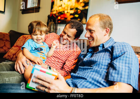 Gay fathers playing with baby son on sofa Stock Photo