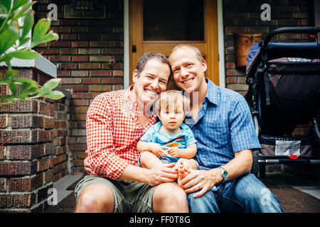 Gay fathers holding baby son on front stoop Stock Photo