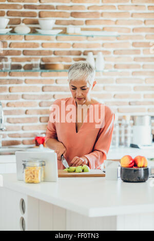 Older Caucasian woman cutting apples in kitchen Stock Photo