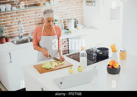 Older Caucasian woman cutting apples in kitchen Stock Photo